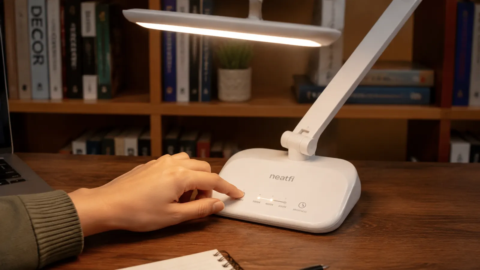 Hand adjusting the touch control panel on an LED desk lamp to change color temperature